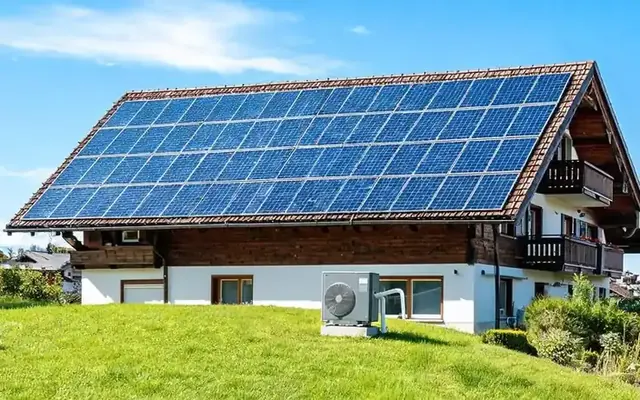 Panneaux solaires photovoltaïques sur le toit d'une maison suisse avec une pompe à chaleur air-eau installée dans le jardin