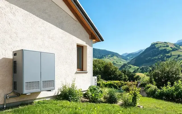 Pompe à chaleur air-eau installée contre la façade d'une villa du canton de Fribourg, collines des Préalpes en arrière-plan